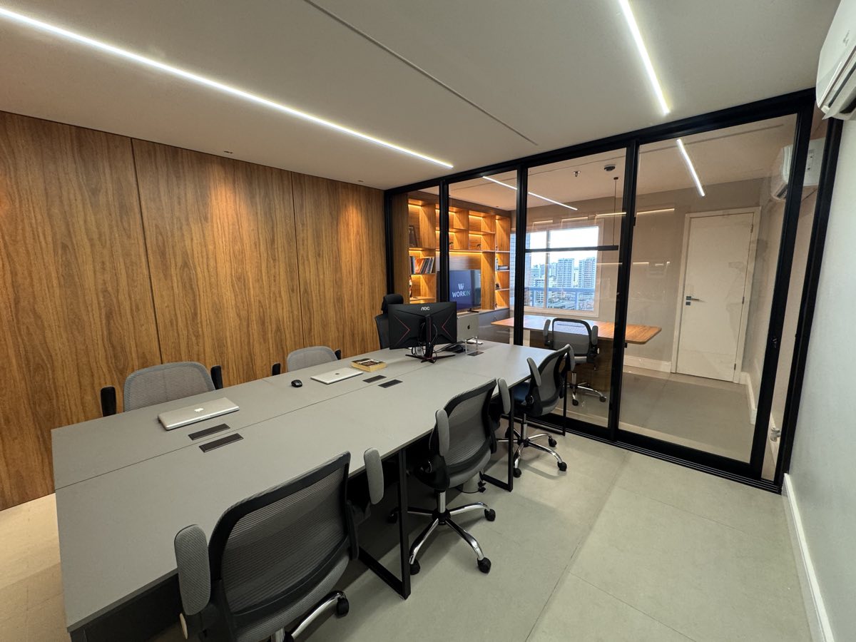 Sala de trabalho com mesa compartilhada e divisória de vidro para a sala de reunião