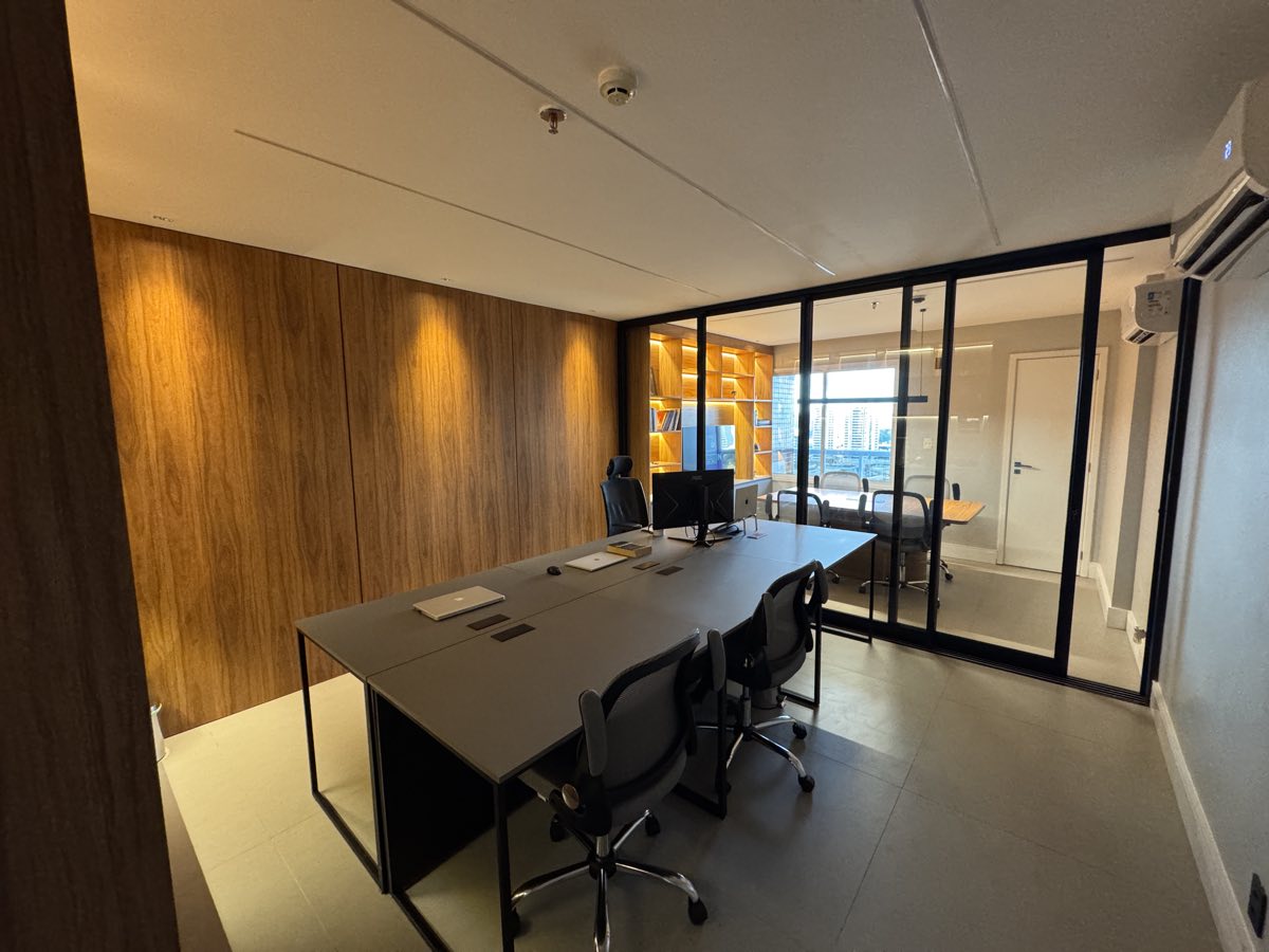 Sala de trabalho vista da porta, com painel de madeira e a sala de reunião ao fundo